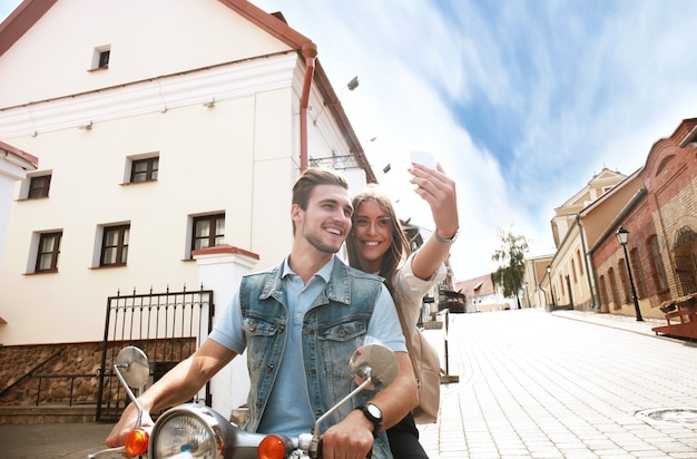 Pareja feliz en scooter haciendo foto selfie en smartphone al aire libre