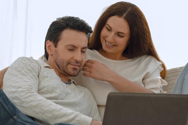 Foto pareja feliz sentada en el sofá en sus brazos mirando la computadora portátil