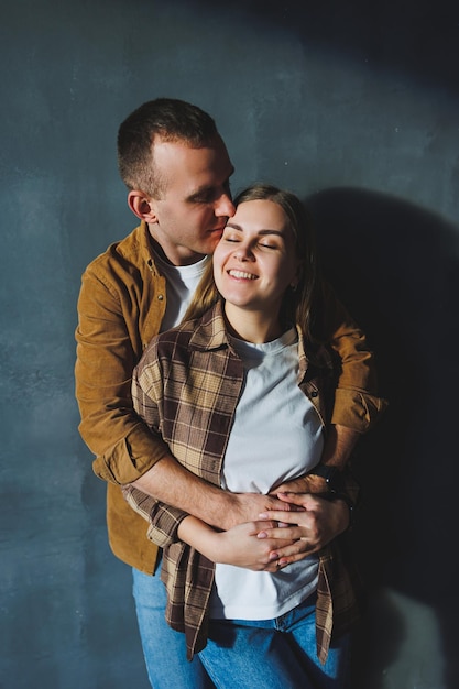 Foto pareja feliz sonriente vestida con jeans y camisas de pie sobre un fondo de pared gris aislado fondo de pared de hormigón gris el concepto de una pareja feliz enamorada