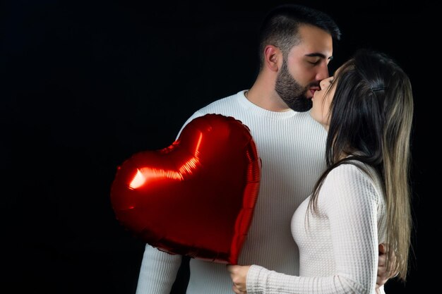 Pareja feliz sosteniendo un globo en forma de corazón rojo mientras se besan