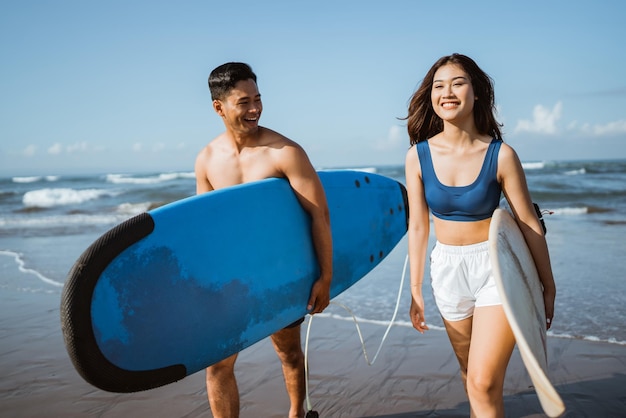 Pareja feliz sosteniendo tablas de surf en la playa con cielo azul en el fondo