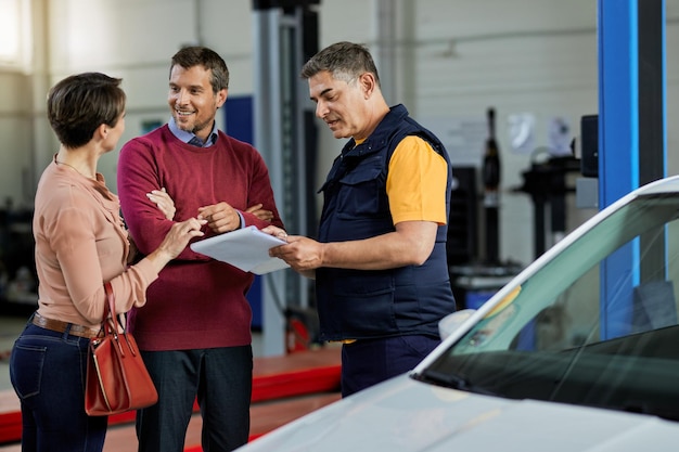 Una pareja feliz y su mecánico de automóviles comunicándose en un taller de reparación de automóviles