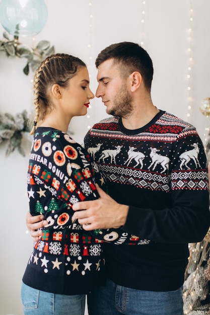 Una pareja feliz con suéter tradicional decorando el árbol de Navidad juntos en casa