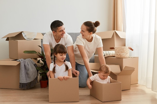 Pareja feliz con sus hijos en cajas de cartón divirtiéndose juntos en un día de mudanza, jugando con niños y expresando amor y felicidad, finalmente comprando su propia casa.