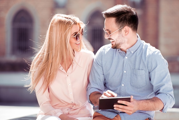 Pareja feliz con tableta sentada al aire libre