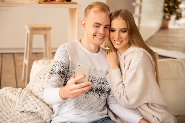 Pareja feliz con teléfono celular en línea felicitando por Navidad. Sonriendo y celebrando las vacaciones de invierno.