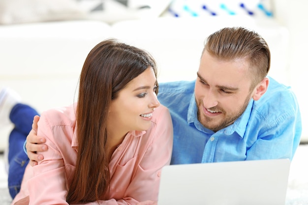 Una pareja feliz tirada en el suelo y trabajando en una laptop