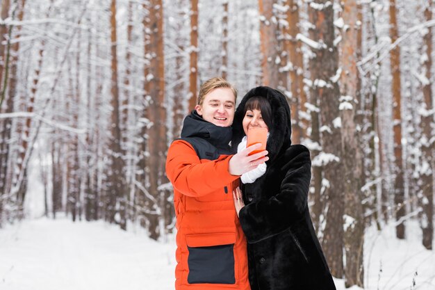 Pareja feliz tomando selfie por teléfono inteligente en invierno.