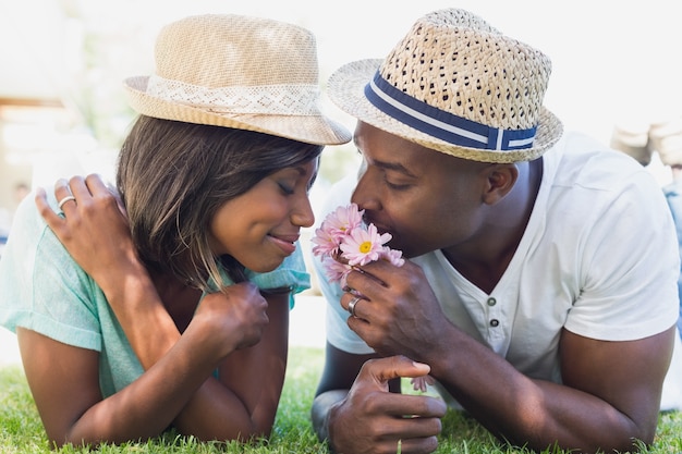 Pareja feliz tumbado en el jardín juntos oliendo flores