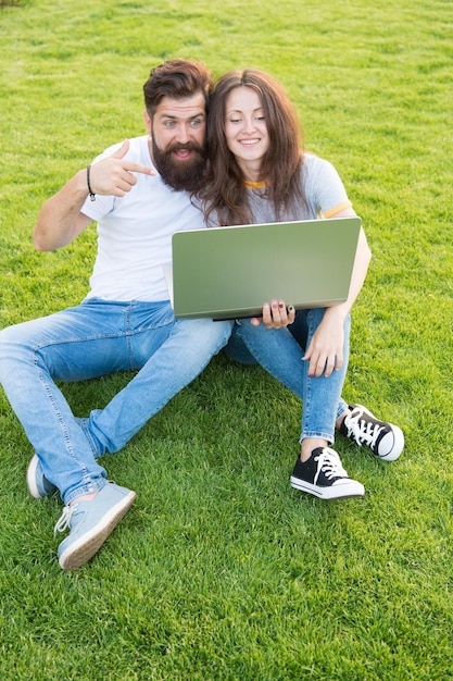 Una pareja feliz usa una computadora portátil en la hierba verde Trabajar al aire libre beneficia trabajar en una computadora en un parque hombre y mujer navegando por internet en una computadora portátil estudiantes vida compras en línea comunicación en línea