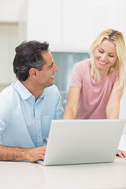 Pareja feliz usando la computadora portátil en la cocina