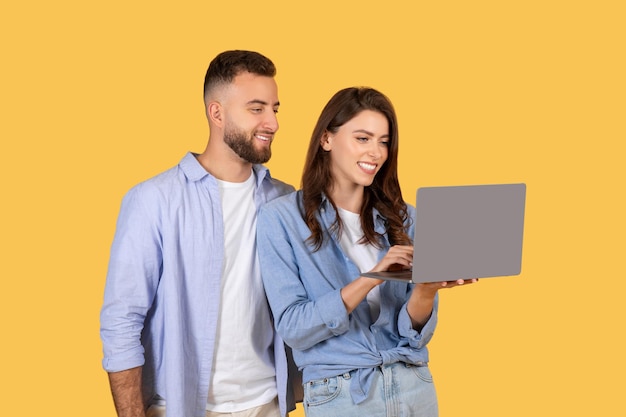 Una pareja feliz usando una computadora portátil juntos en un fondo amarillo