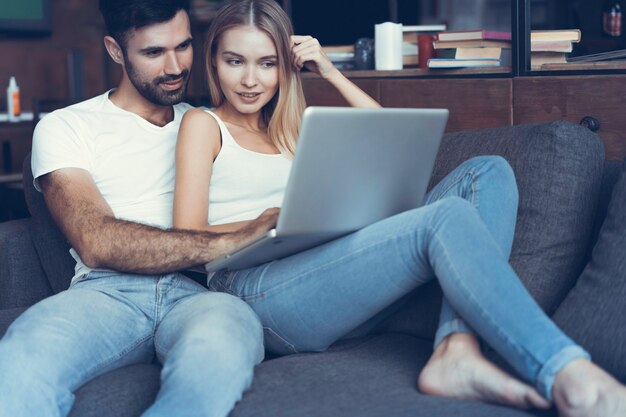 Pareja feliz usando una computadora portátil en el sofá.