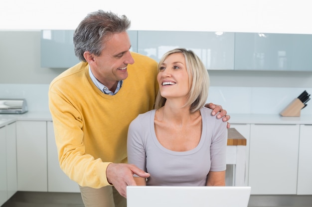 Pareja feliz usando laptop en cocina