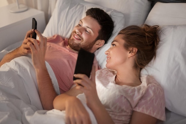 pareja feliz usando teléfonos inteligentes en la cama por la noche