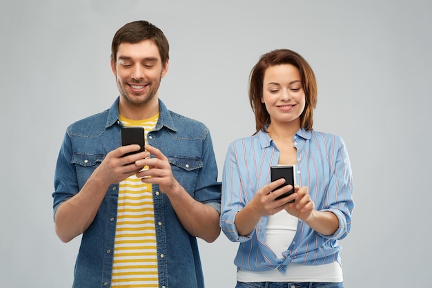 pareja feliz usando teléfonos inteligentes sobre gris