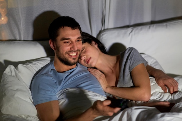 pareja feliz viendo la televisión en la cama por la noche en casa