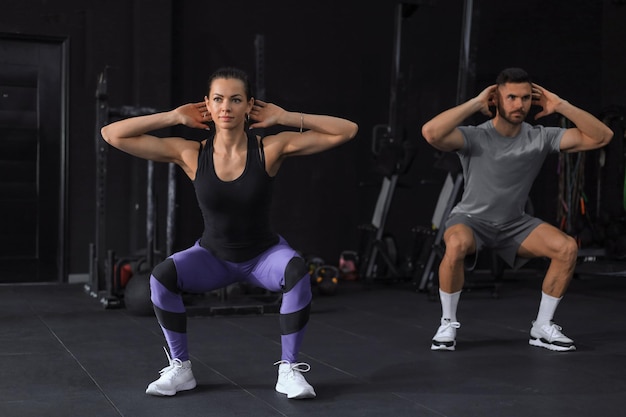 Foto pareja de fitness en ropa deportiva haciendo ejercicios en cuclillas en el gimnasio
