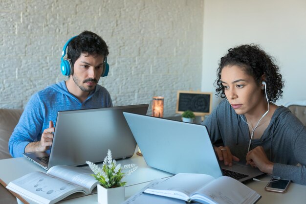 Foto una pareja de freelancers enfocados con auriculares trabajando en una computadora portátil dentro de la casa en la habitación de iving