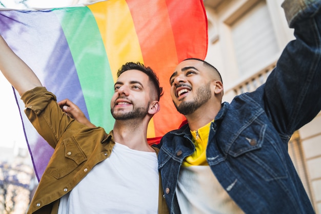 Pareja gay abrazando y mostrando su amor con la bandera del arco iris.