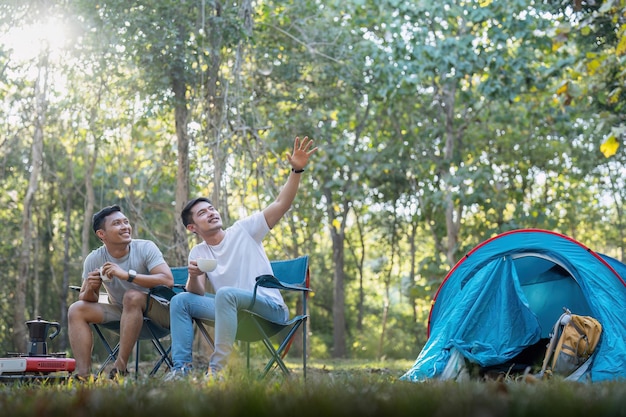Pareja gay asiática viajando con carpa acampando al aire libre y varios estilos de vida de aventura caminatas vacaciones de verano activas bebiendo café y hablando juntos.