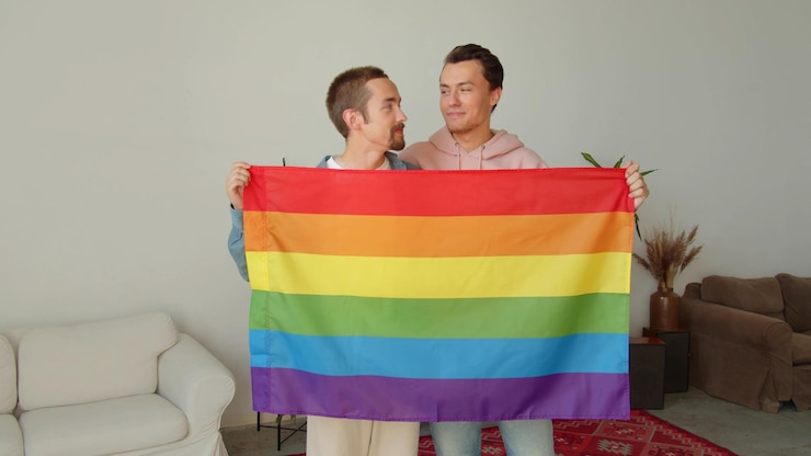 Foto una pareja gay con una bandera arco iris contra la pared