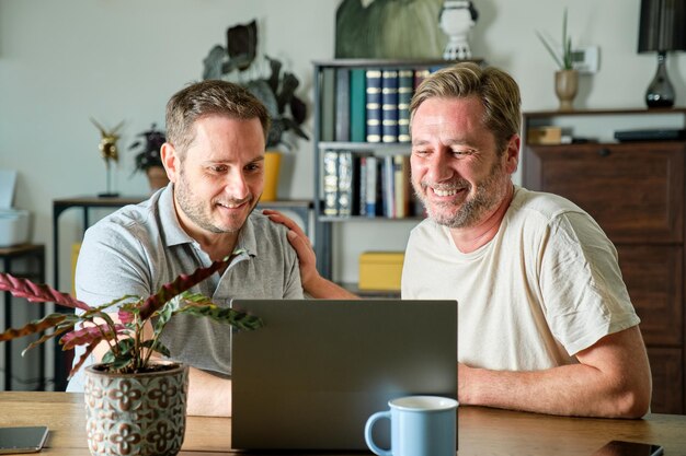 Una pareja gay de chicos maduros sonriendo en la terraza de su casa abrazándose