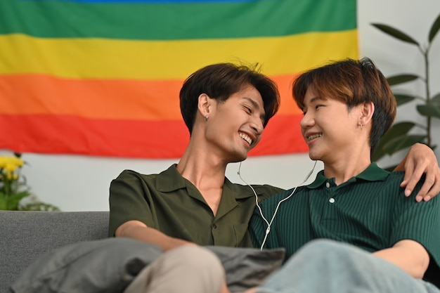 Pareja gay masculina despreocupada escuchando música en auriculares pasando tiempo juntos en casa Relación LGBT y concepto de vida confortable