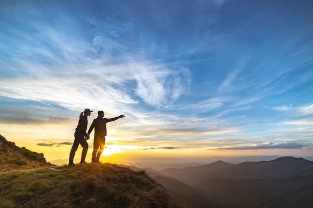 La pareja gesticulando en la montaña con una pintoresca puesta de sol
