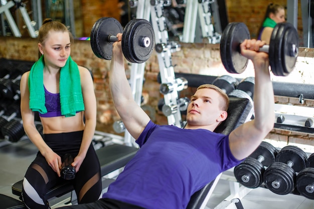 Pareja en el gimnasio Un entrenador personal le explica a una joven ejercicios con una mancuerna