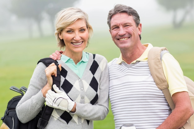 Pareja de golf sonriendo y sosteniendo clubes