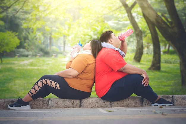 Pareja gorda bebiendo agua en las aceras del parque