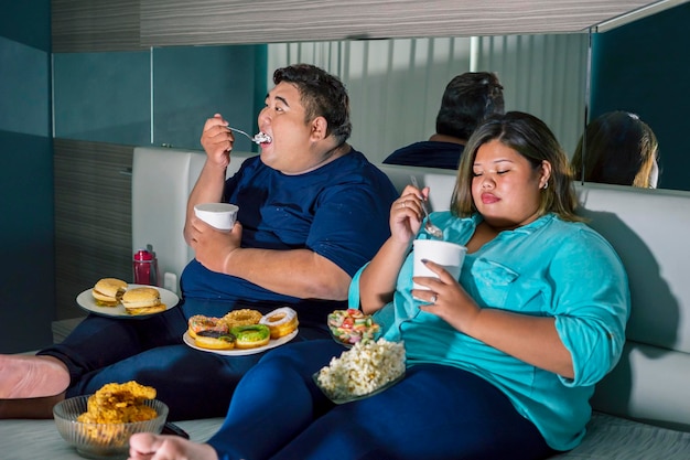 Pareja gorda comiendo helado mientras ve la televisión