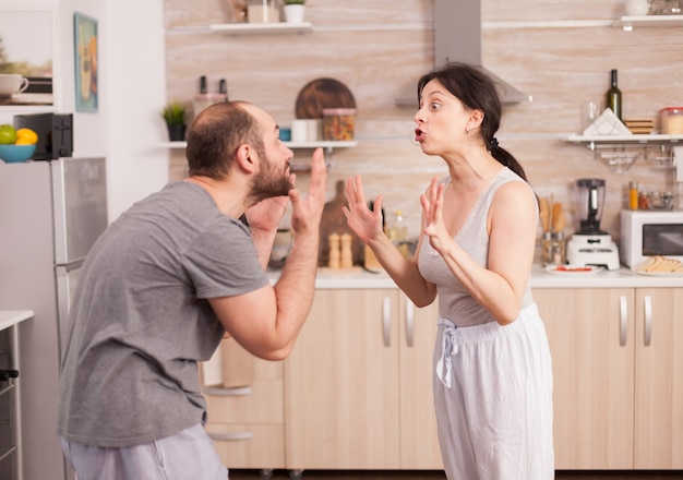 Pareja gritándose el uno al otro en la cocina por la mañana. Peleas de la joven pareja en la cocina. El hombre y la mujer gritan de frustración durante la conversación en casa.