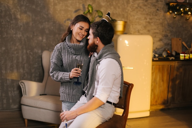 Foto pareja hablando sobre el novio y la novia de los amantes de la víspera de año nuevo se comunican muy bien en la habitación decorada de forma festiva. chica sostiene una copa de champán en las manos.