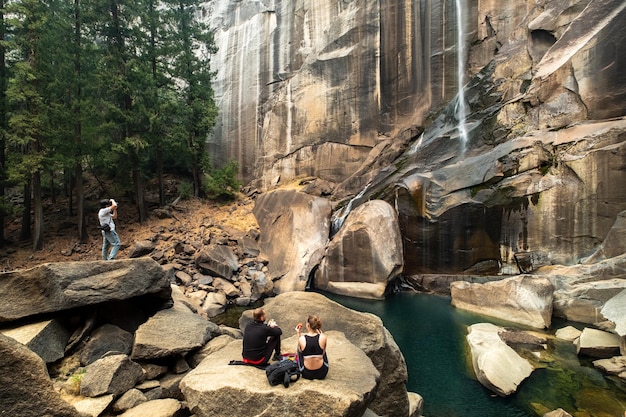 Una pareja hace un picnic frente a Vernal Falls mientras un hombre toma una foto en la cascada Yosemite