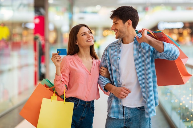 Pareja haciendo compras con tarjeta de crédito y bolsas en hipermercado