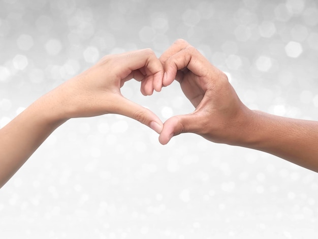 Foto pareja haciendo forma de corazón con la mano en el brillante fondo bokeh