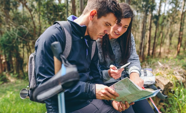 Foto pareja haciendo trekking sentada mirando móvil y mapa