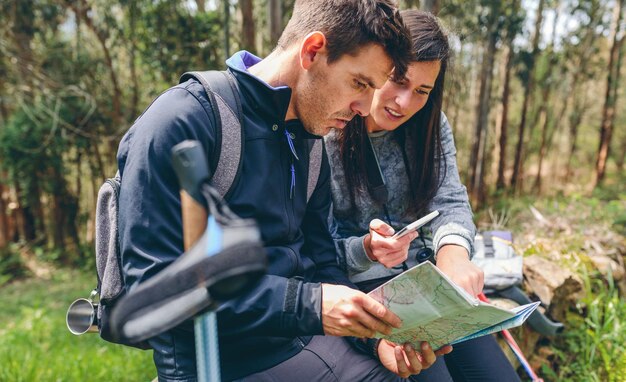 Pareja haciendo trekking sentada mirando móvil y mapa