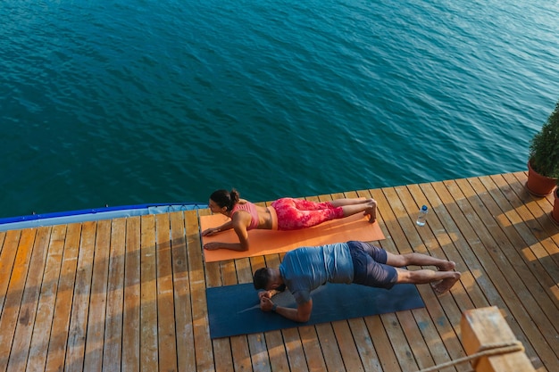 Pareja haciendo yoga cerca del lago temprano en la mañana