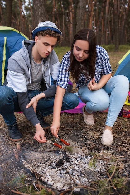 Pareja hambrienta asa salchichas en la hoguera. Romance turístico. Estilo de vida de camping.