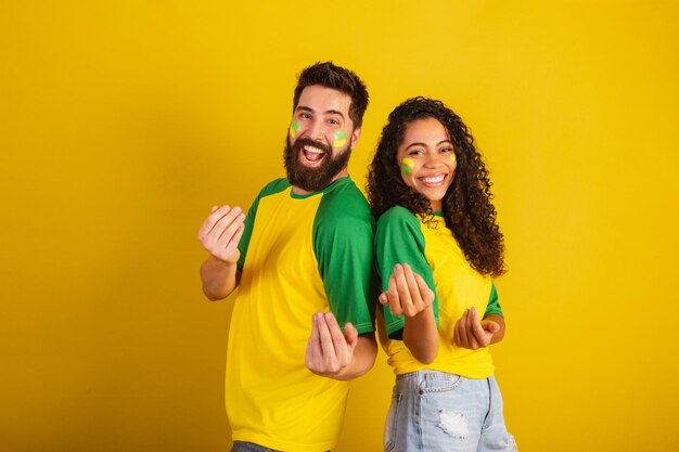 Pareja de hinchas de fútbol de brasil vestidos con los colores de la nación mujer negra hombre caucásico invitando con las manos