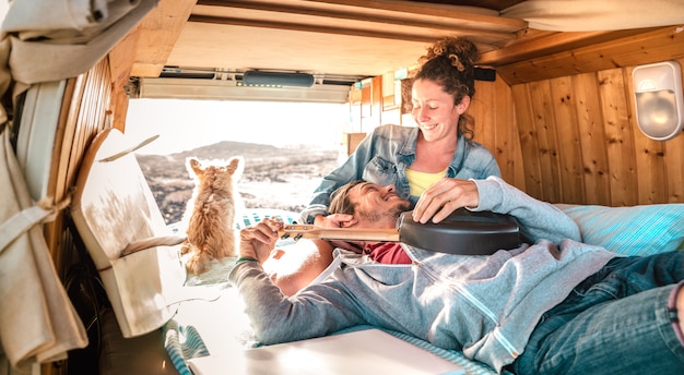 Pareja hippie amd perro viajando juntos en transporte van vintage al atardecer