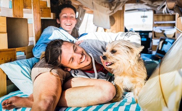 Pareja hippie con perro gracioso viajando juntos en transporte minivan vintage