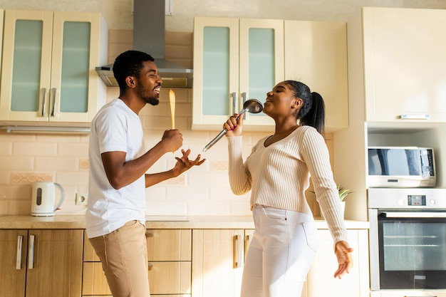 Pareja hispana cantando juntos sosteniendo un cucharón como un micrófono en la cocina