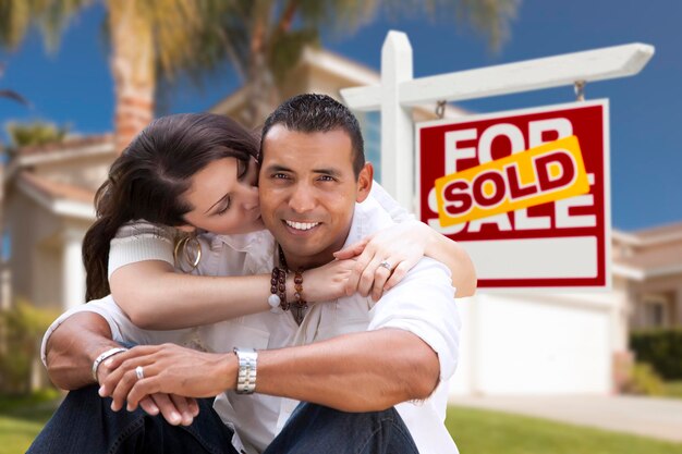 Una pareja hispana compra una casa nueva y vende un cartel de bienes raíces