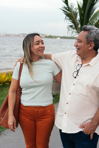 Pareja hispana de mediana edad sonriendo felizmente y abrazándose mientras está de pie en el parque