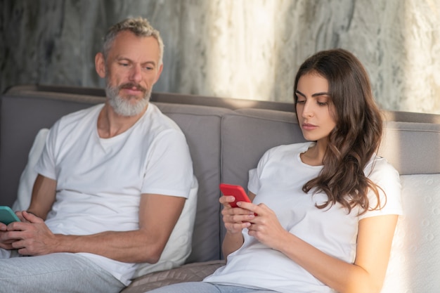 Pareja. Un hombre mirando a su esposa mientras ella usa un teléfono inteligente