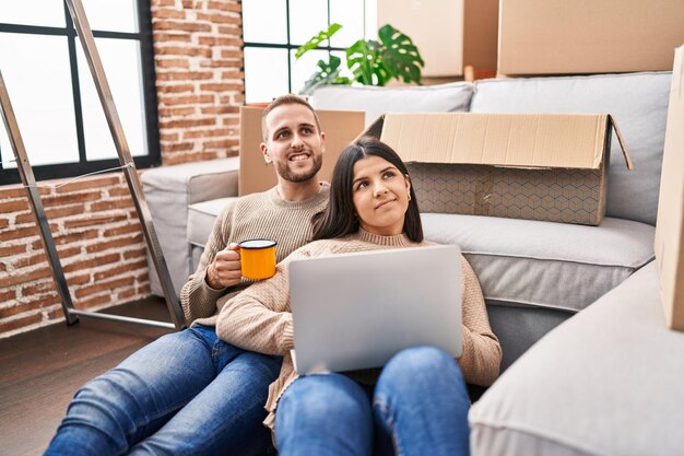 Pareja de hombre y mujer bebiendo café usando una computadora portátil en un nuevo hogar